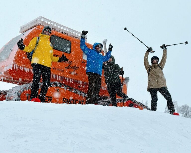 Four people cheering while wearing snowshoes in front of a snowcat machine in the winter